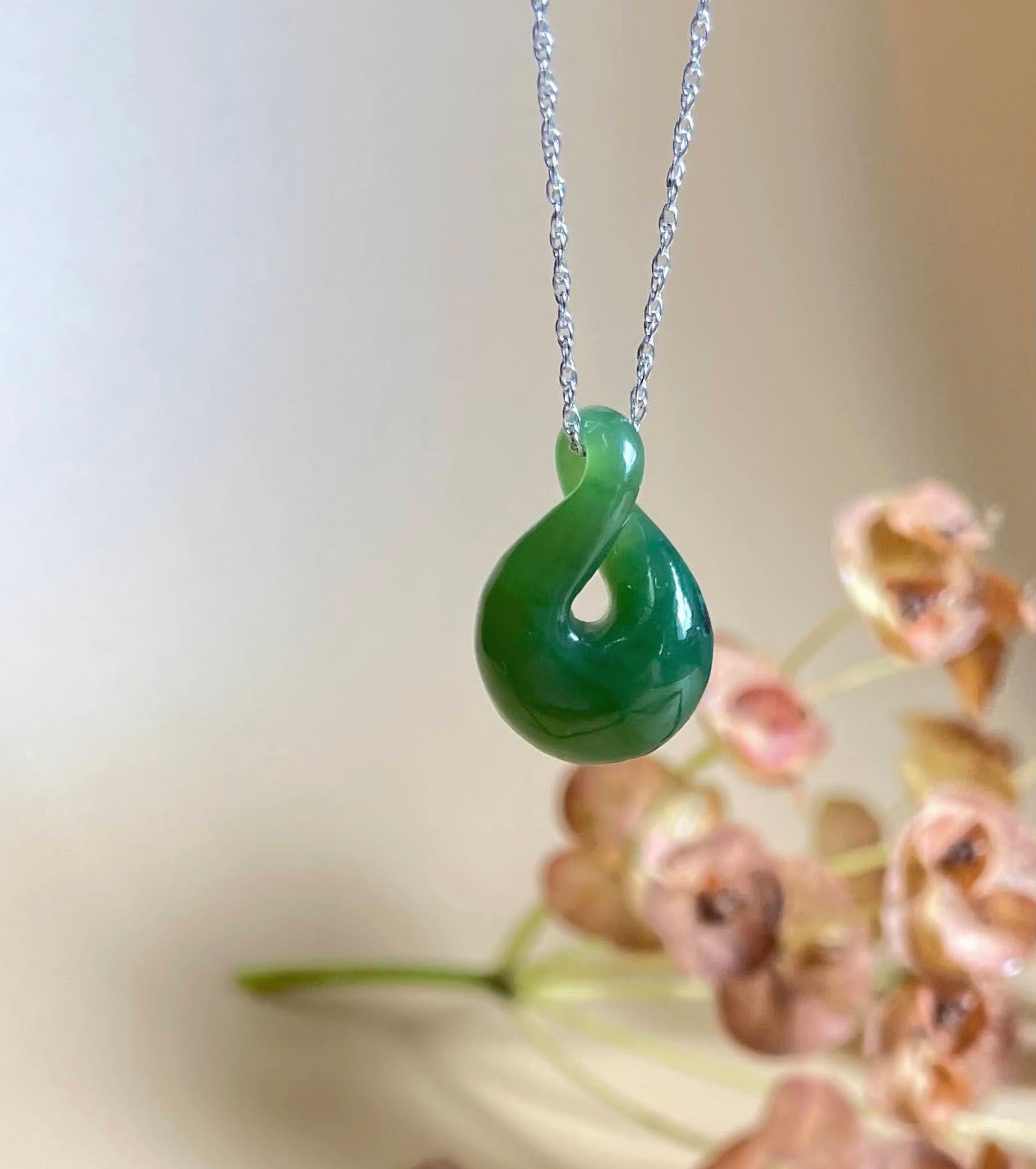 Green jade pendant with a looping teardrop shape hanging from a silver chain