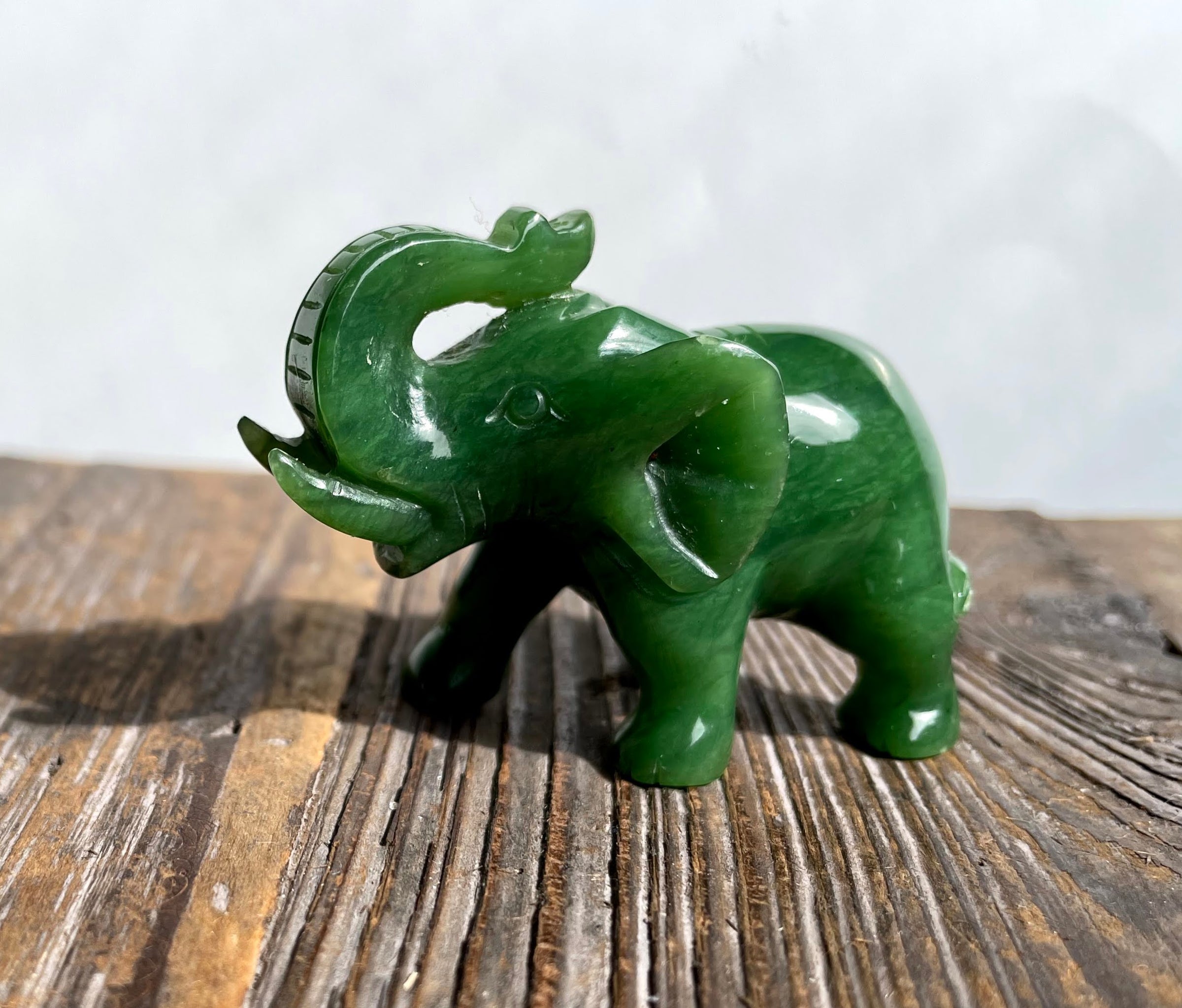 Green jade elephant carving with raised trunk standing on a weathered wooden surface.