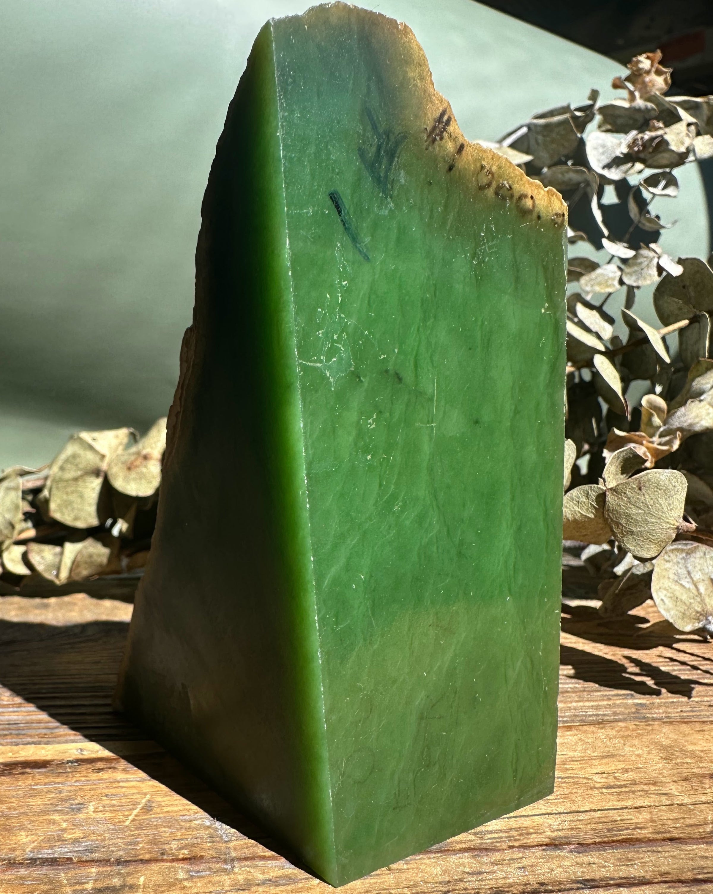 Tall Wyoming jade rough block with brown rind on a wooden surface