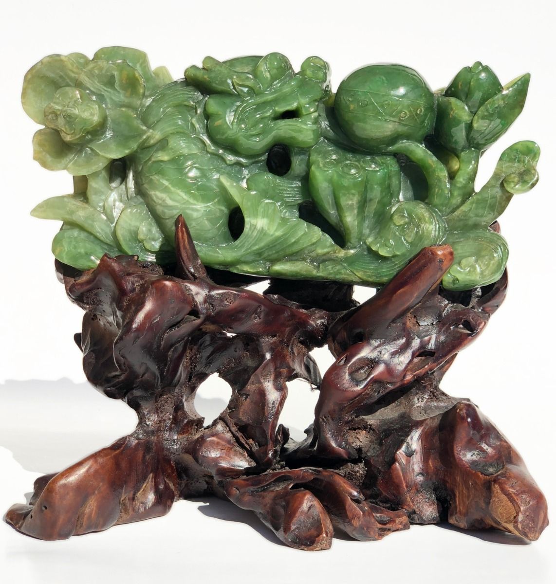 Green jade tree sculpture perched on a dark carved wooden base