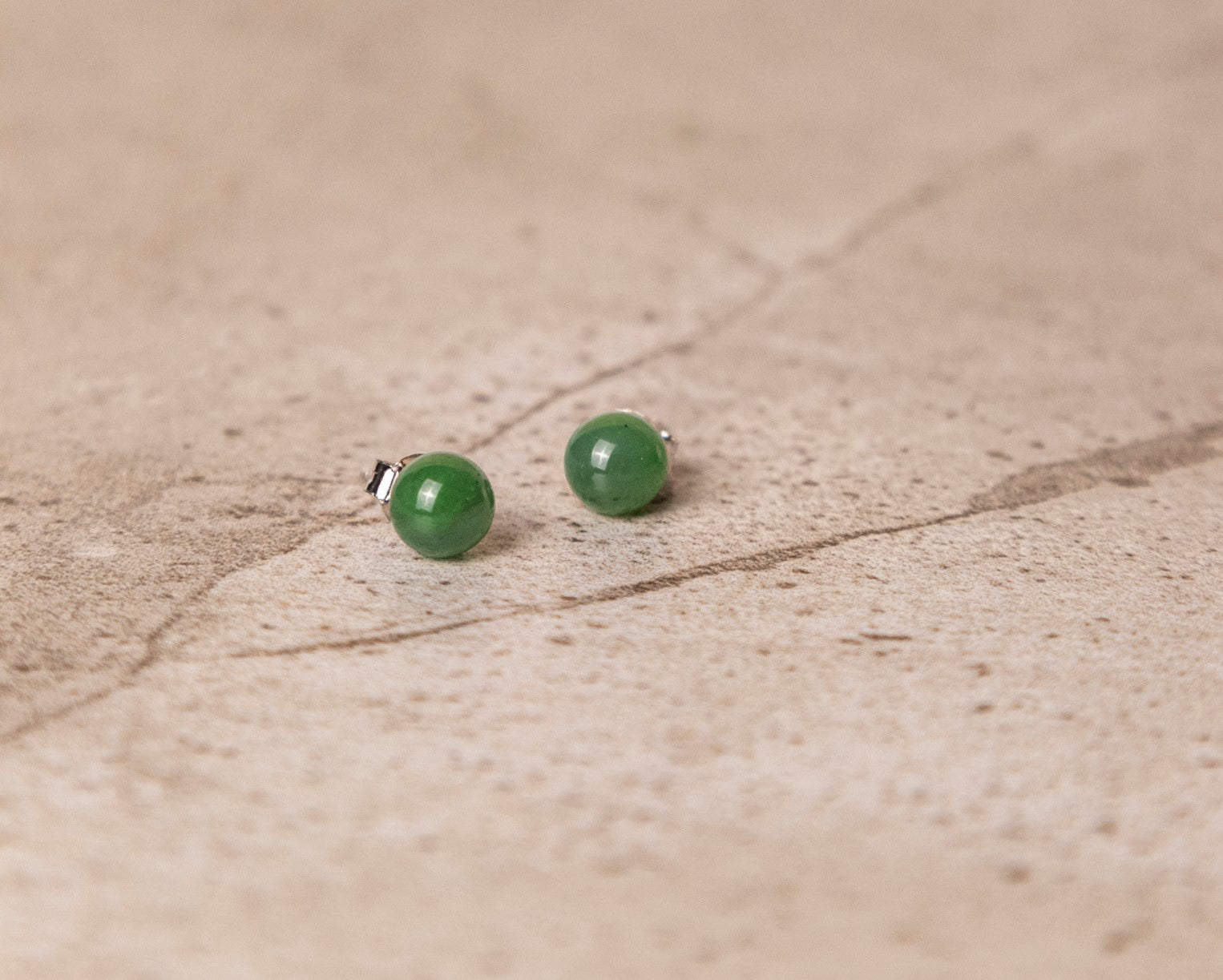 Green jade bead stud earrings on a beige textured surface.