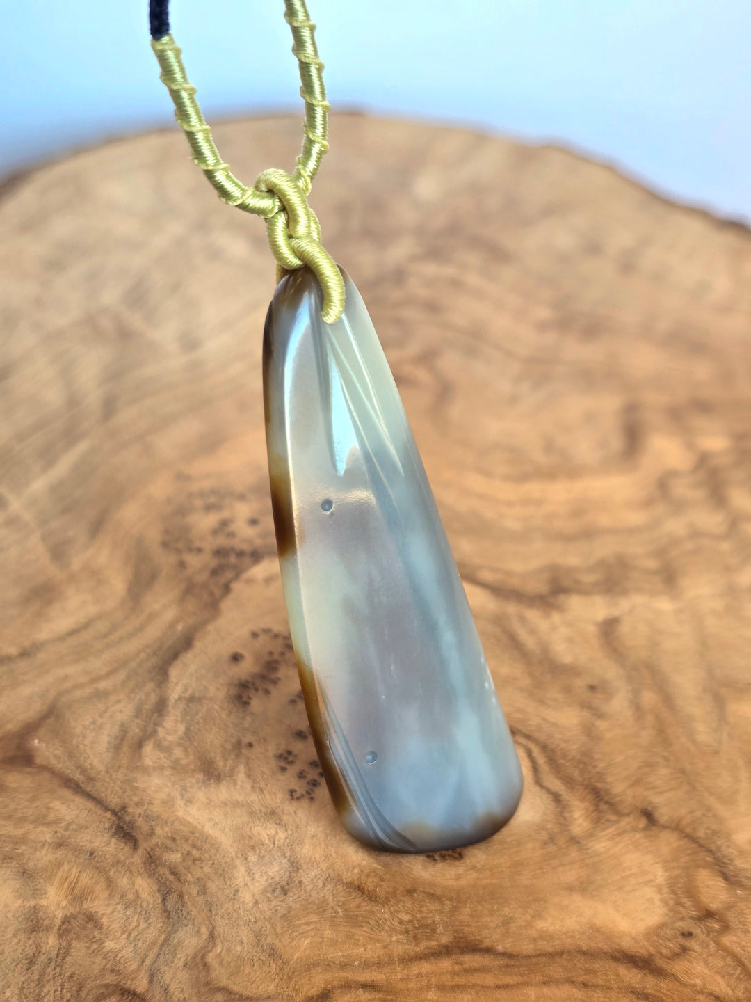 Side view of jade pendant with yellow wrapped cord knot against a rocky desert backdrop