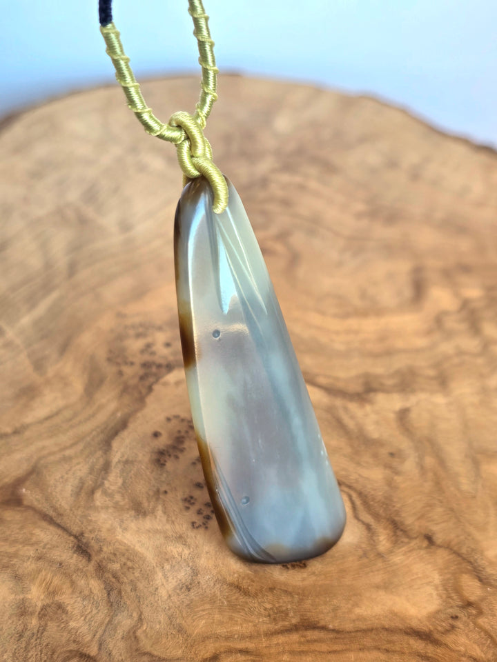 Side view of jade pendant with yellow wrapped cord knot against a rocky desert backdrop