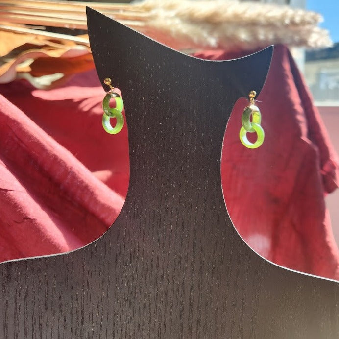 Green jade infinity hoop earrings hanging on a dark wooden display stand.