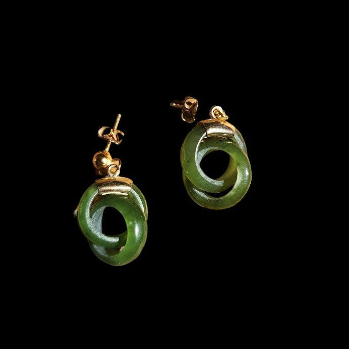 Green jade infinity hoop earrings with gold posts photographed on a black background.