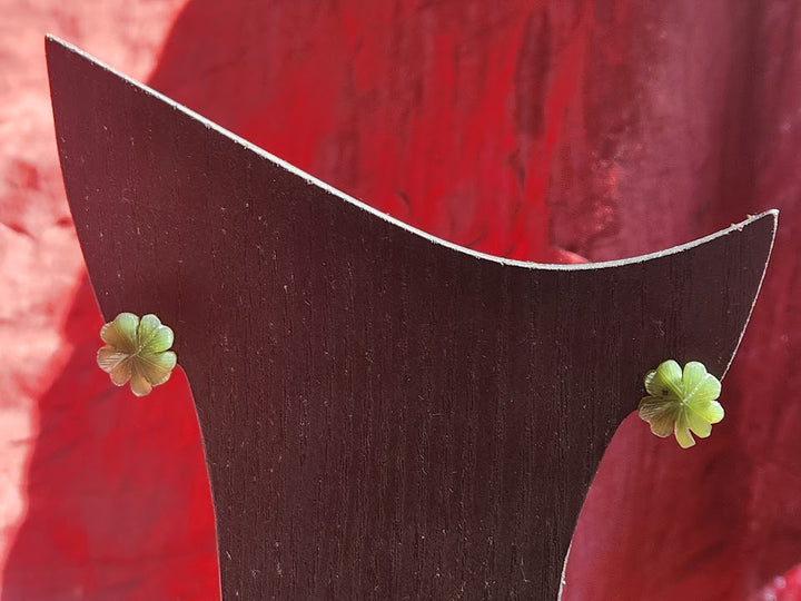 Pair of green jade shamrock stud earrings on a dark curved display stand.