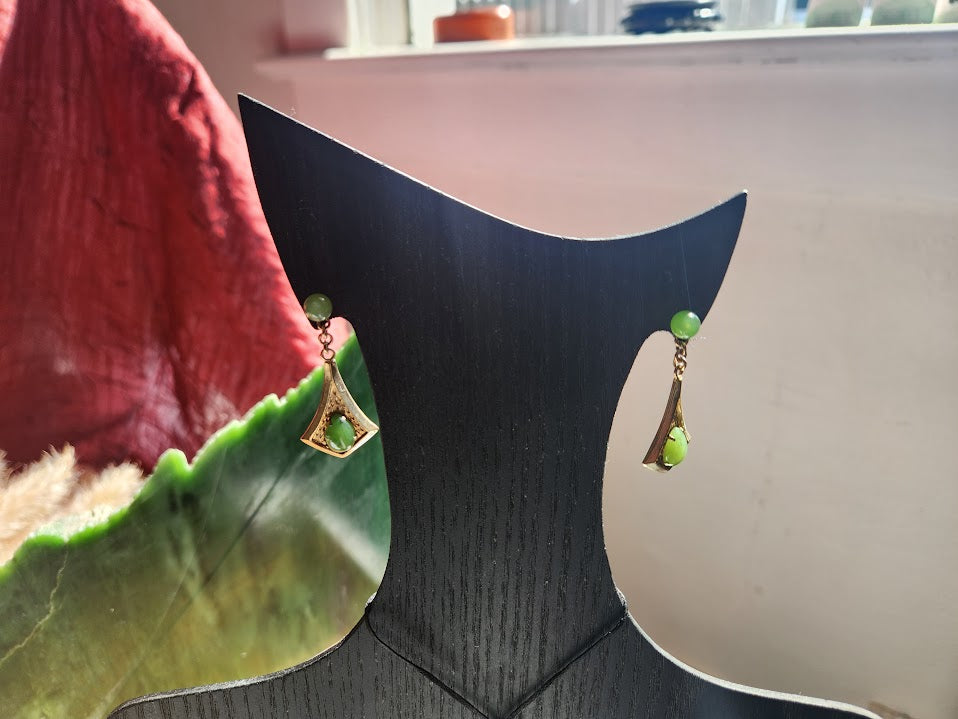 Vintage Jade Drop Earrings hanging from a curved black display stand with green jade drops