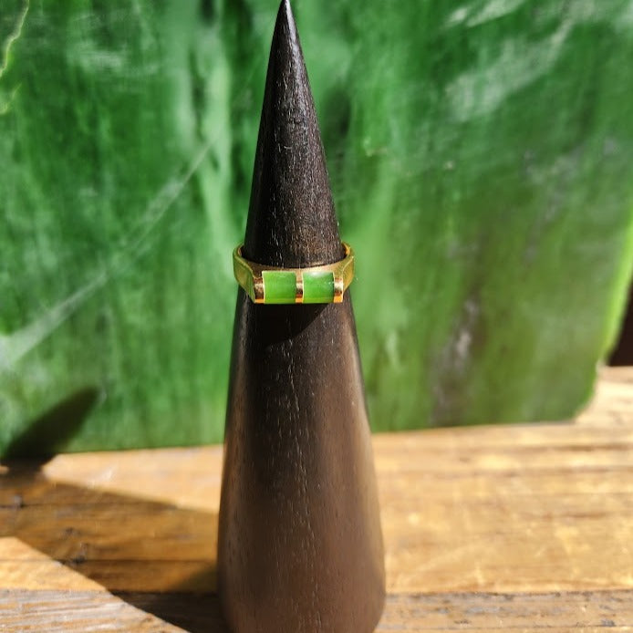 Vintage jade ring with two lime green rectangular inlays on a gold band displayed on a dark cone stand.
