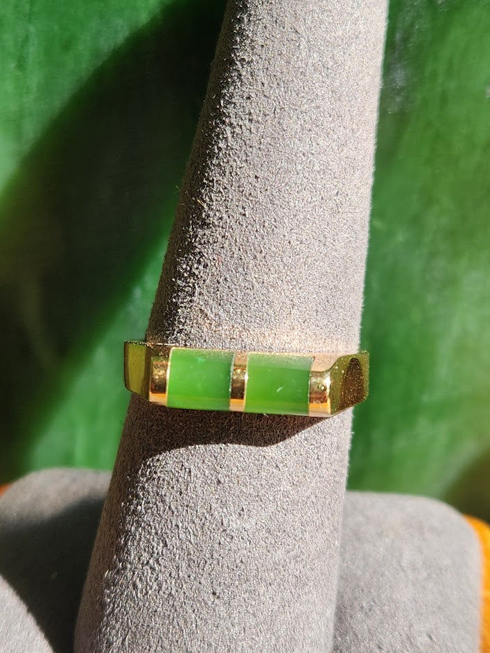 Close up of the jade ring showing lime green rectangular inlays in a gold band on a gray display cone.