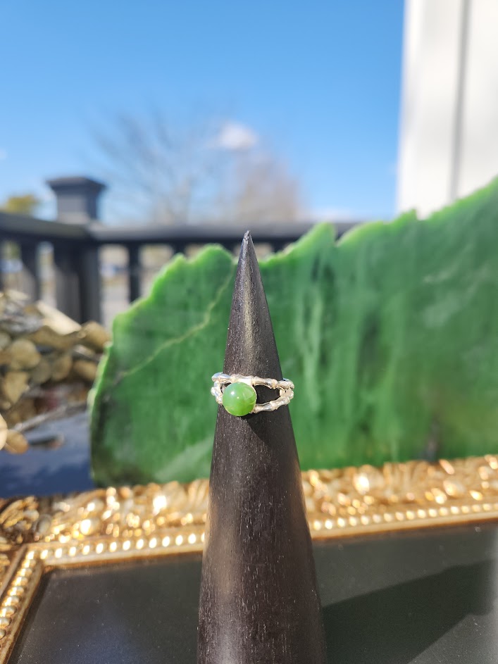 Green jade ring with twin textured silver bands centered on a black display cone
