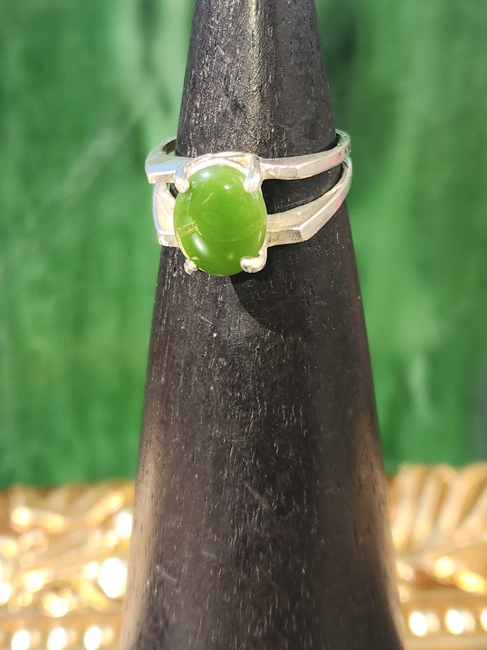 Green jade cabochon set in a silver double-band ring displayed on a black cone stand