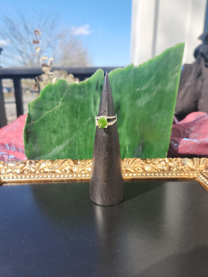 Silver jade ring with a green stone centered on a black display cone outdoors