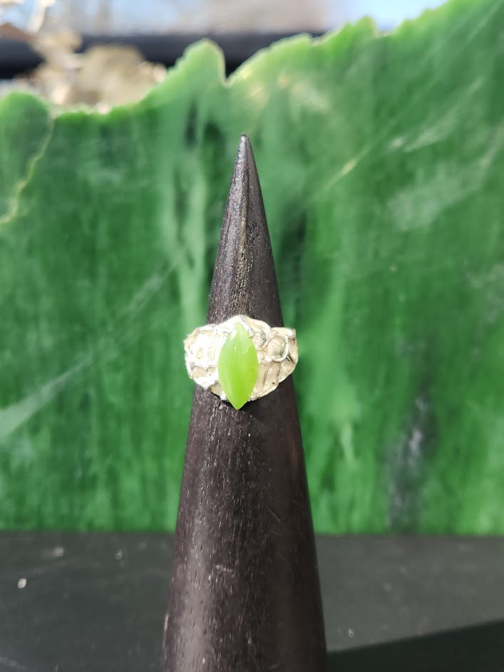 Close up of hammered silver ring with lime green jade on a cone against a green backdrop