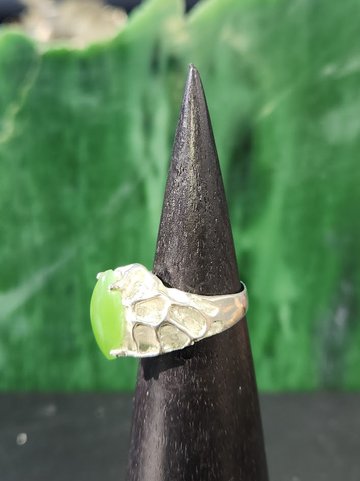 Side view of hammered silver ring with lime jade centerpiece on a dark display cone