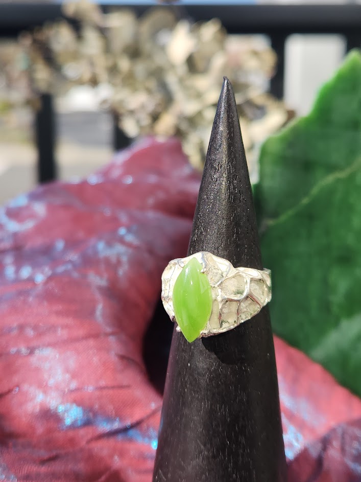 Hammered silver ring with a bright lime jade centerpiece displayed on a dark cone