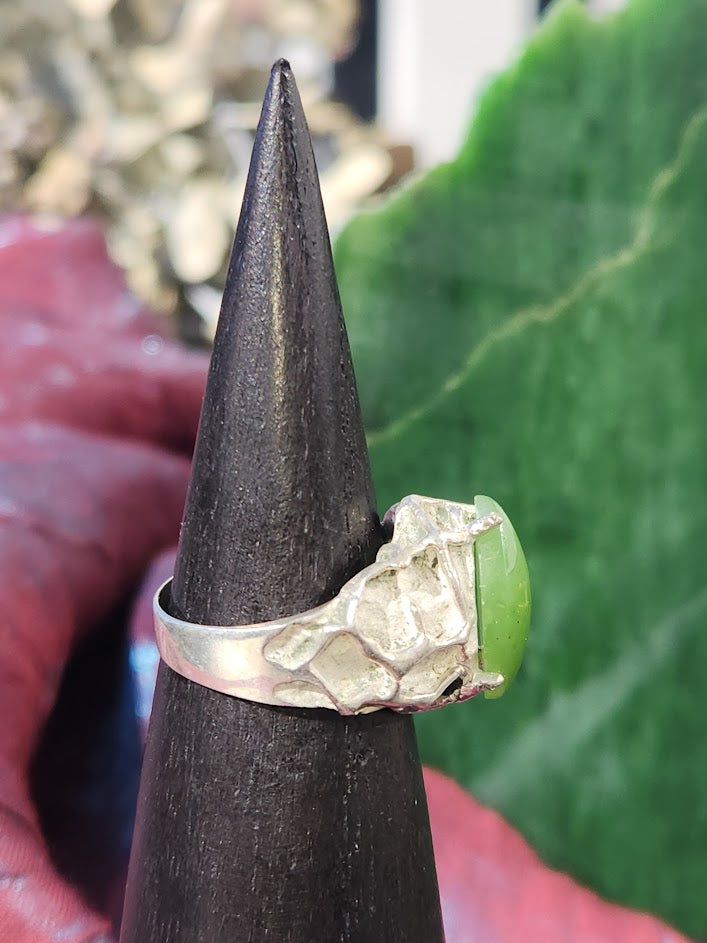 Hammered silver ring with a bright green jade cabochon on a black display cone.