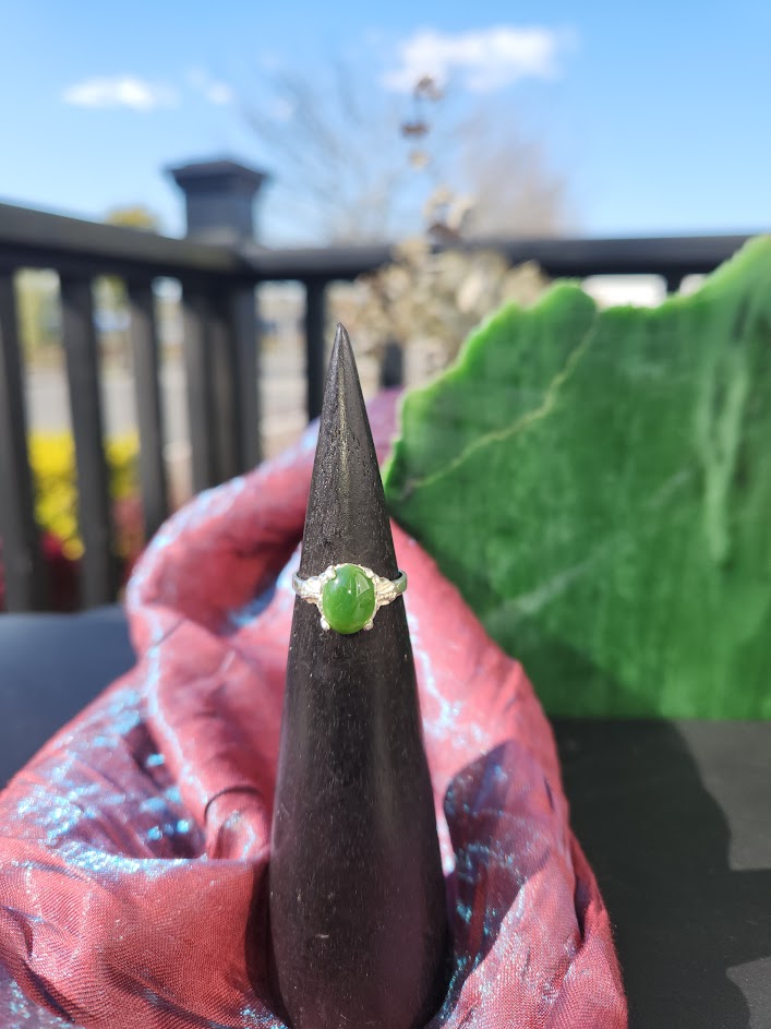 Jade ring displayed on a black cone stand with a vivid green jade stone and detailed silver band