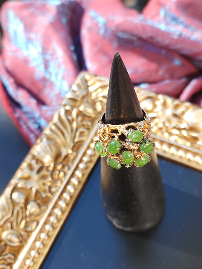 Side view of an ornate gold ring with a cluster of green jade beads on a black display cone
