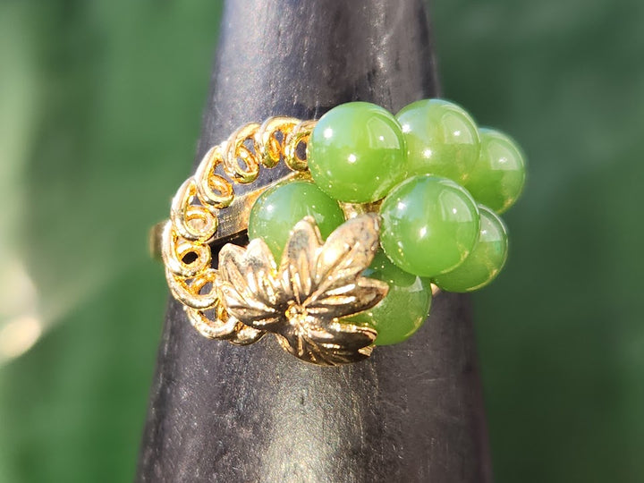 Close-up of Jade grape ring showing gold band and leaf accent encircling green beads.