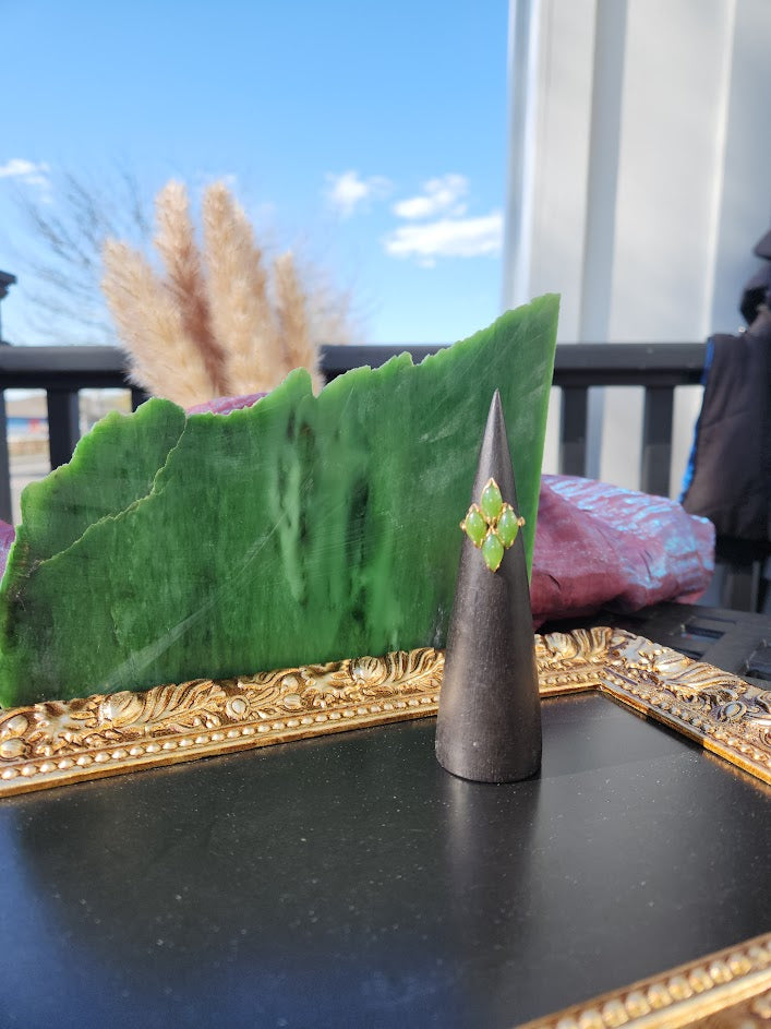 Vintage jade ring on a black cone stand with a green jade cluster and a green backdrop