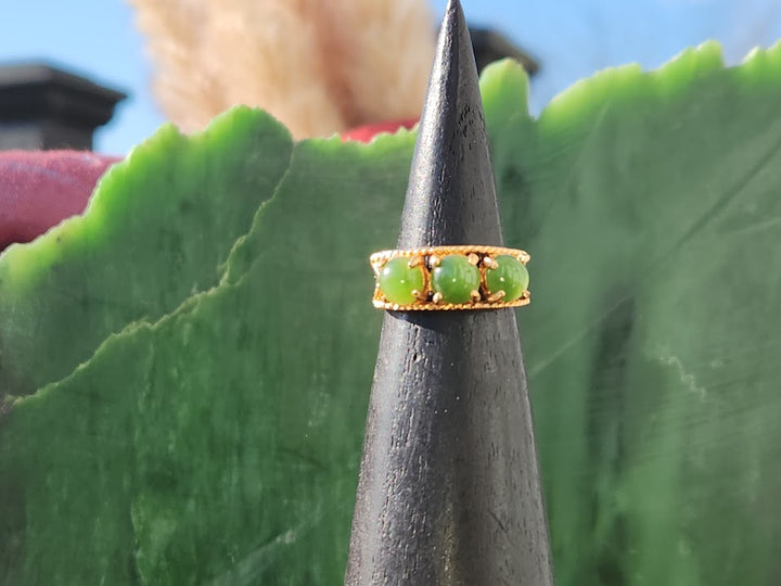 Three green jade beads set in a gold band shown on a display cone with a blurred background