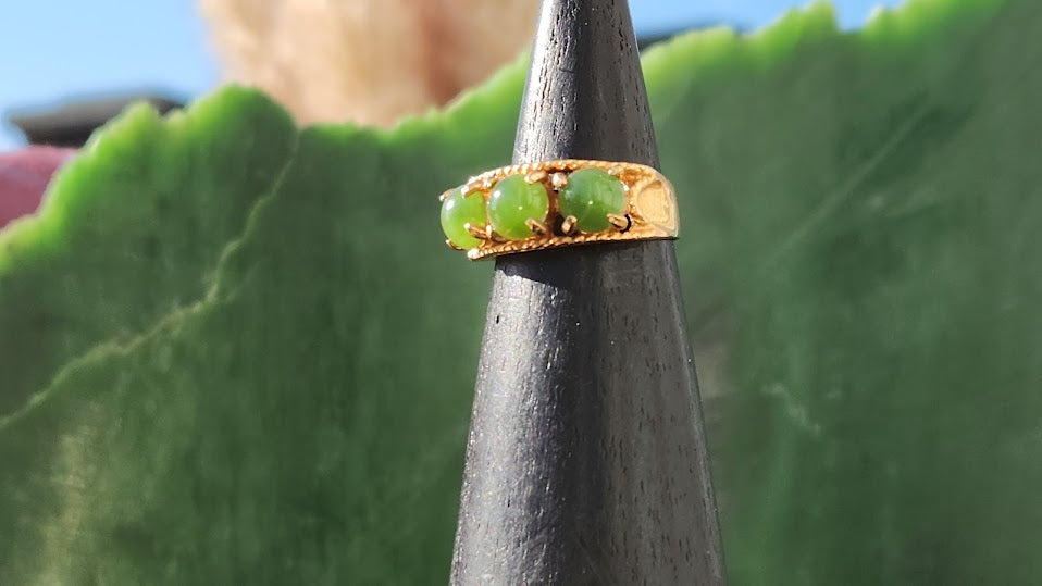 Gold vintage ring with three round green jade beads set along the band on a dark display