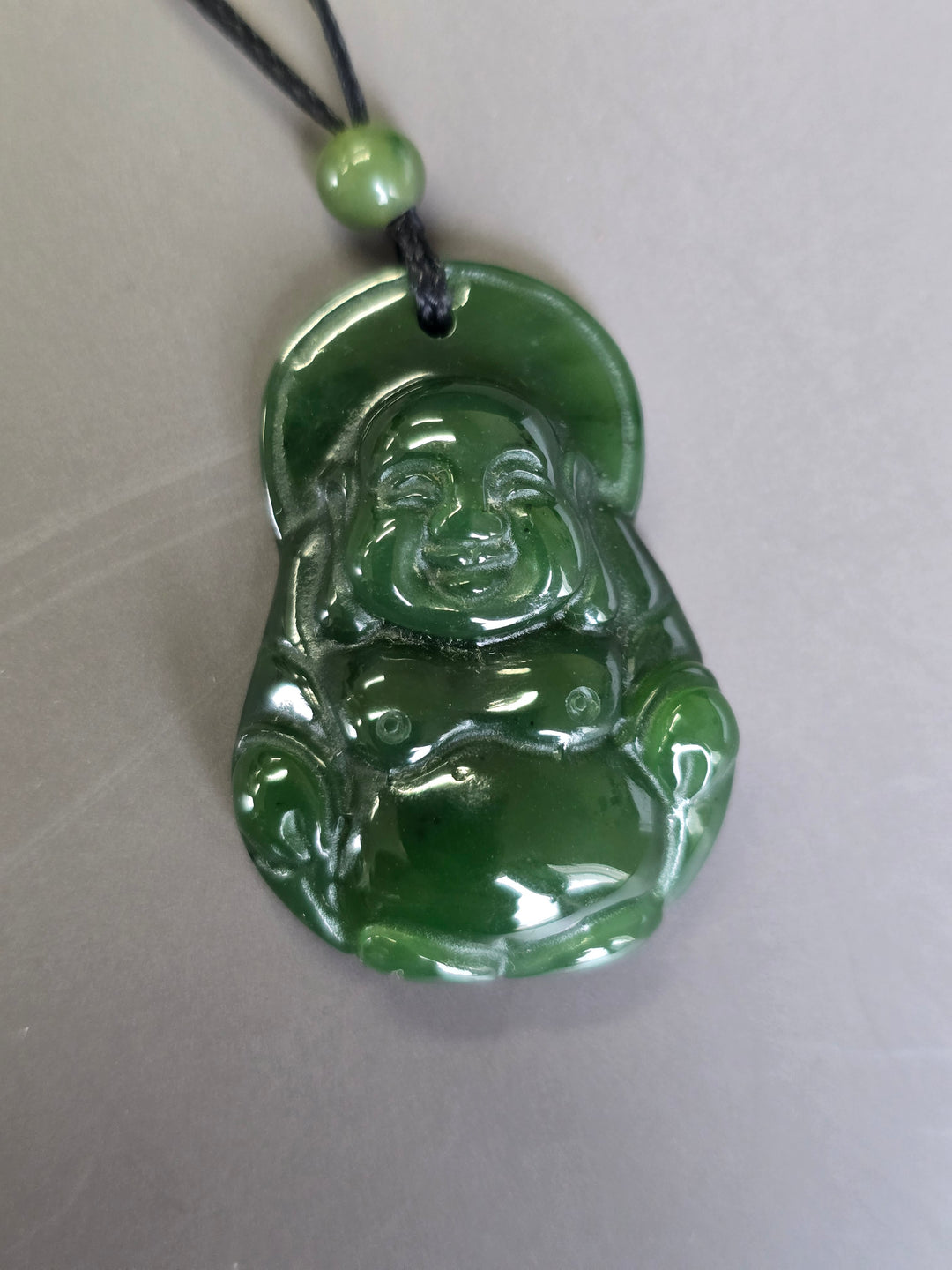 Green jade Laughing Buddha pendant with a circular halo behind the head on a black cord and green bead