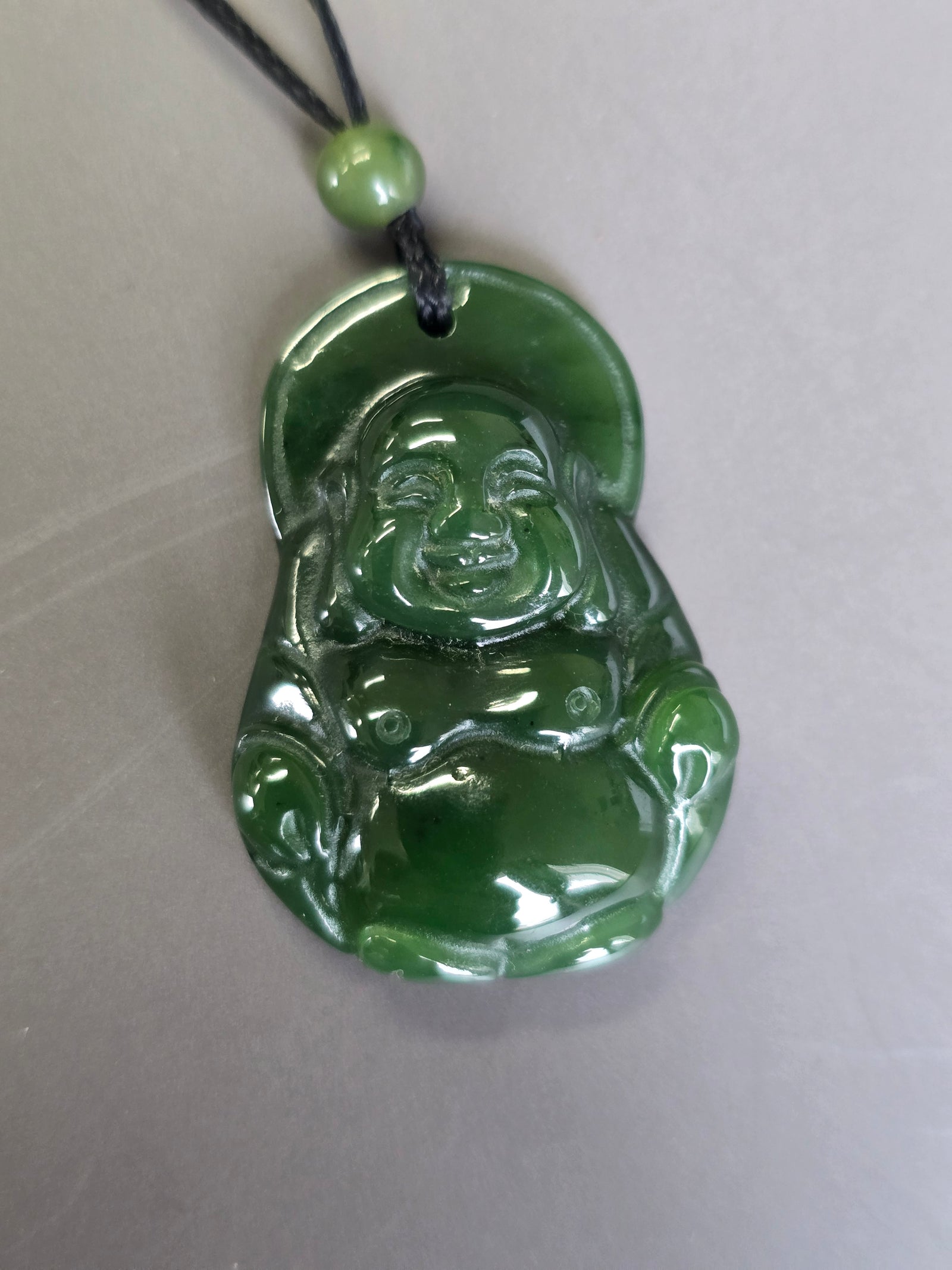 Green jade Laughing Buddha pendant with a circular halo behind the head on a black cord and green bead