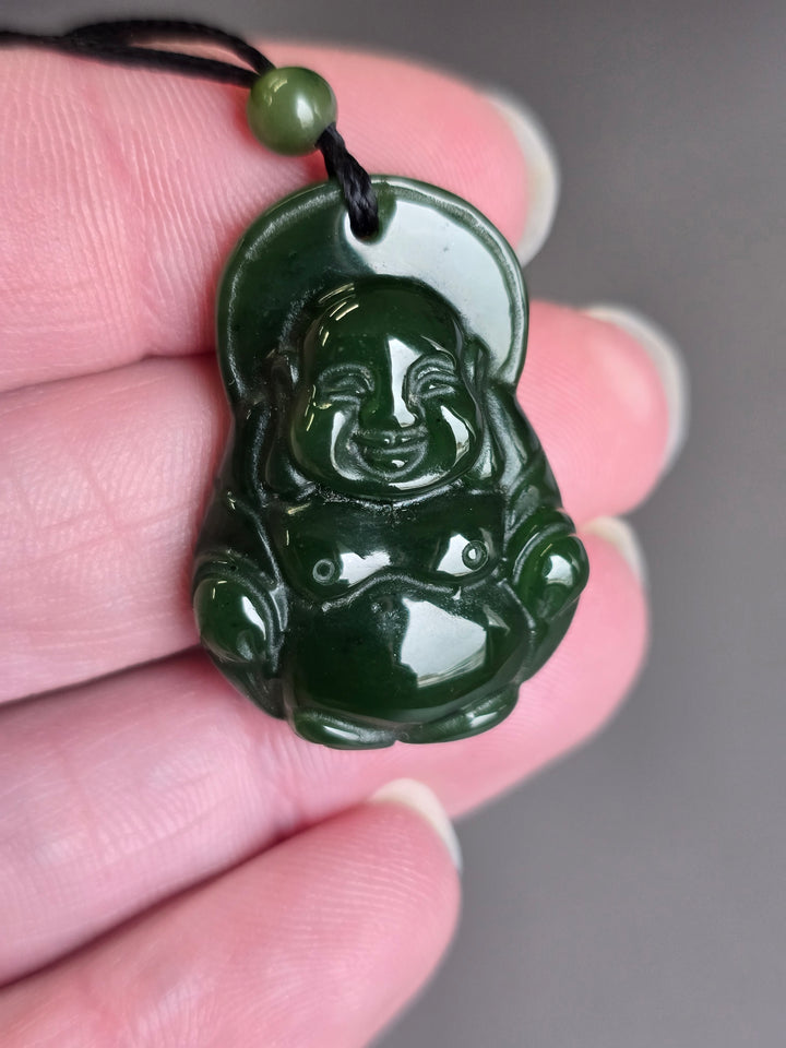 Close-up of the green jade Laughing Buddha pendant held between fingers, highlighting its glossy carved surface