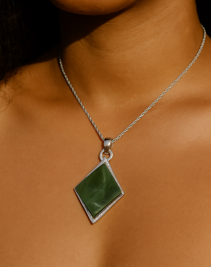 Diamond-shaped green jade pendant on a silver chain worn at the collarbone.