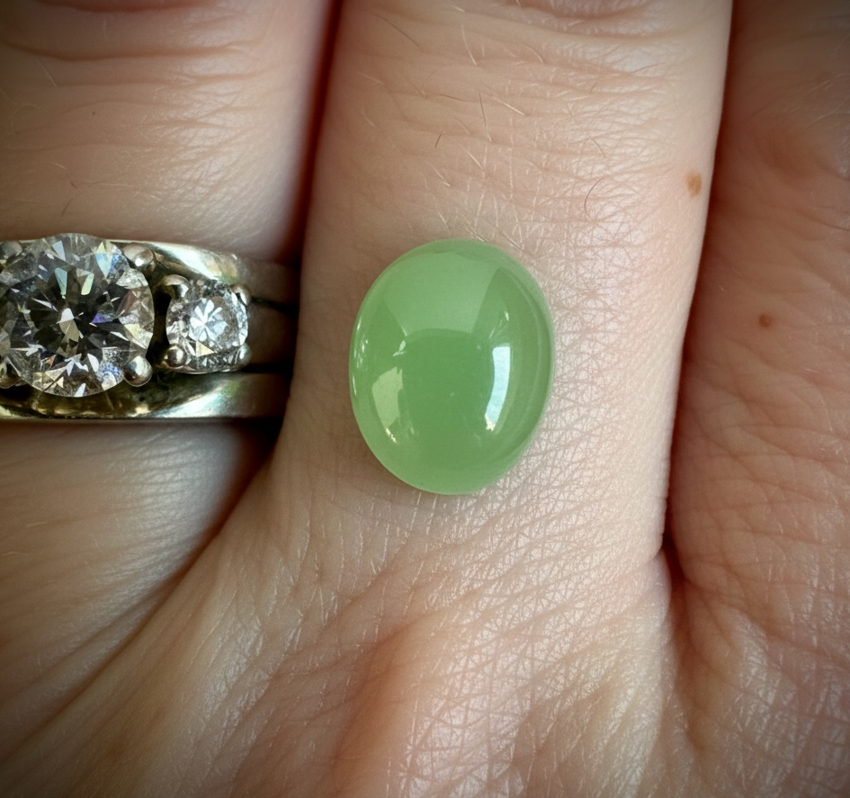 Apple green oval cabochon on a finger beside a diamond ring.