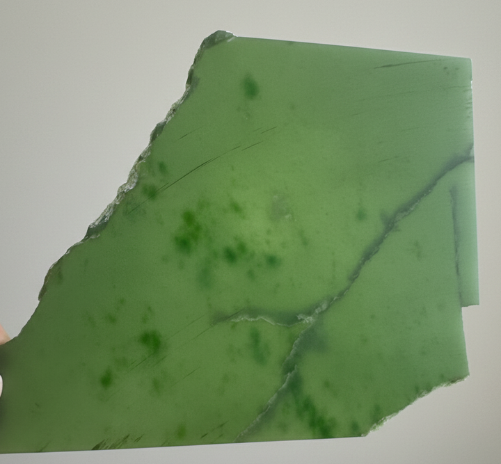 A+ Siberian nephrite jade slab in bright green with a jagged left edge and dark green specks.