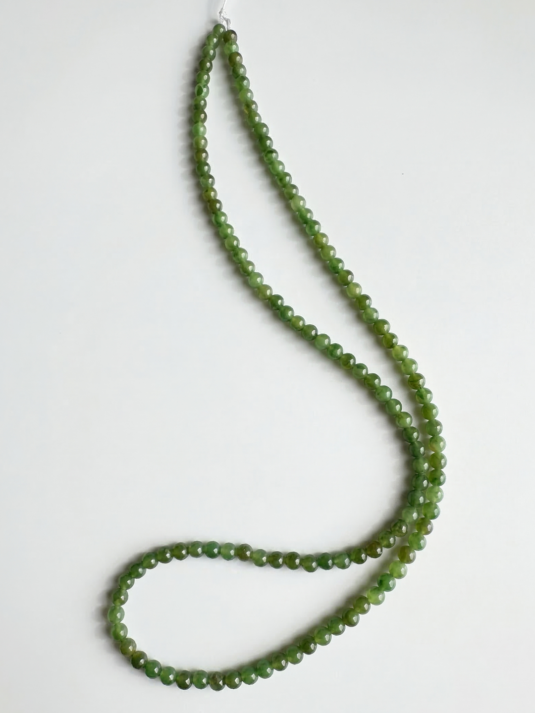 Green nephrite jade beads on white background formed into a long unstrung strand
