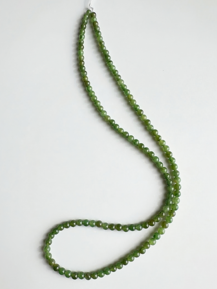 Green nephrite jade beads on white background formed into a long unstrung strand