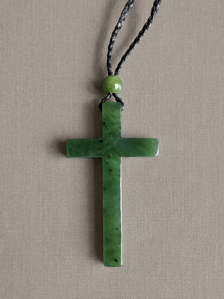 Green jade cross pendant on a braided black cord with a round green bead above it.
