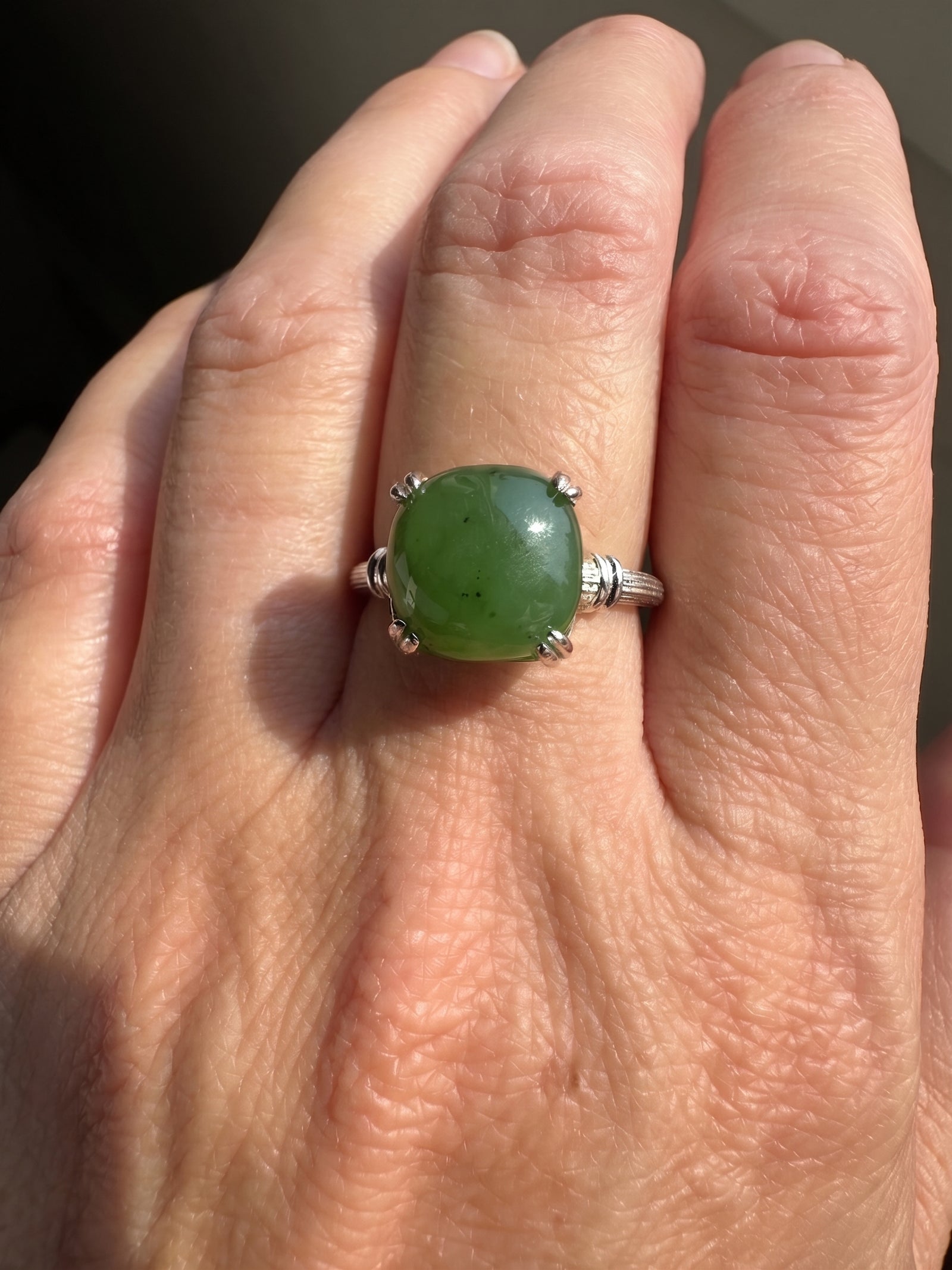 A close-up of a hand wearing a silver ring with a round green cabochon gemstone.