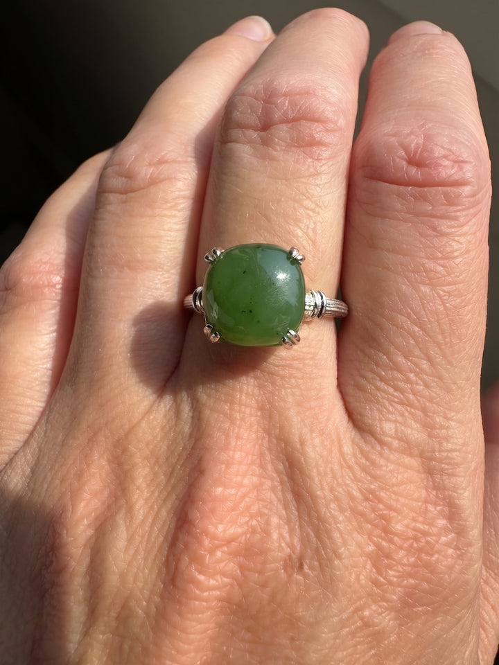 A close-up of a hand wearing a silver ring with a round green cabochon gemstone.