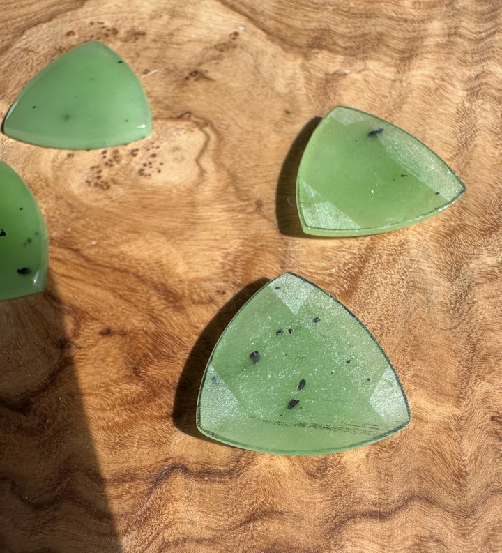 Apple green Siberian jade cabochons triangular with rounded corners on a wood surface, showing small black specks.
