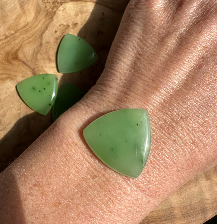 Single apple green Siberian jade cabochon resting on a hand for scale