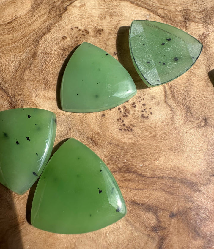 Four apple green Siberian jade cabochons in teardrop shapes arranged on a wood surface