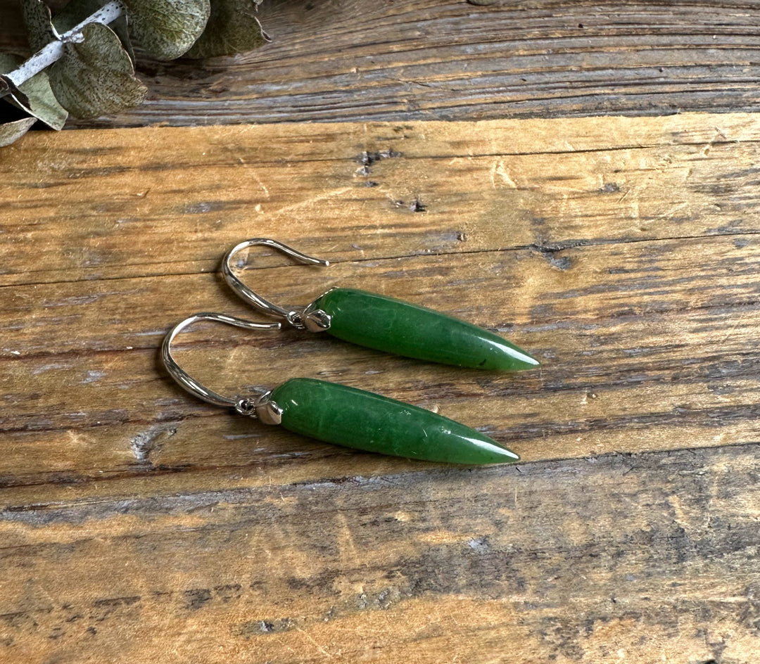 Green jade drop earrings with silver hooks resting on rustic wood surface.