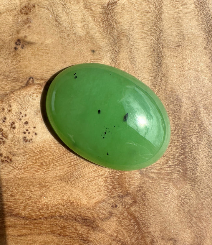 Apple green Siberian cabochon 30x22mm glossy oval resting on wood surface