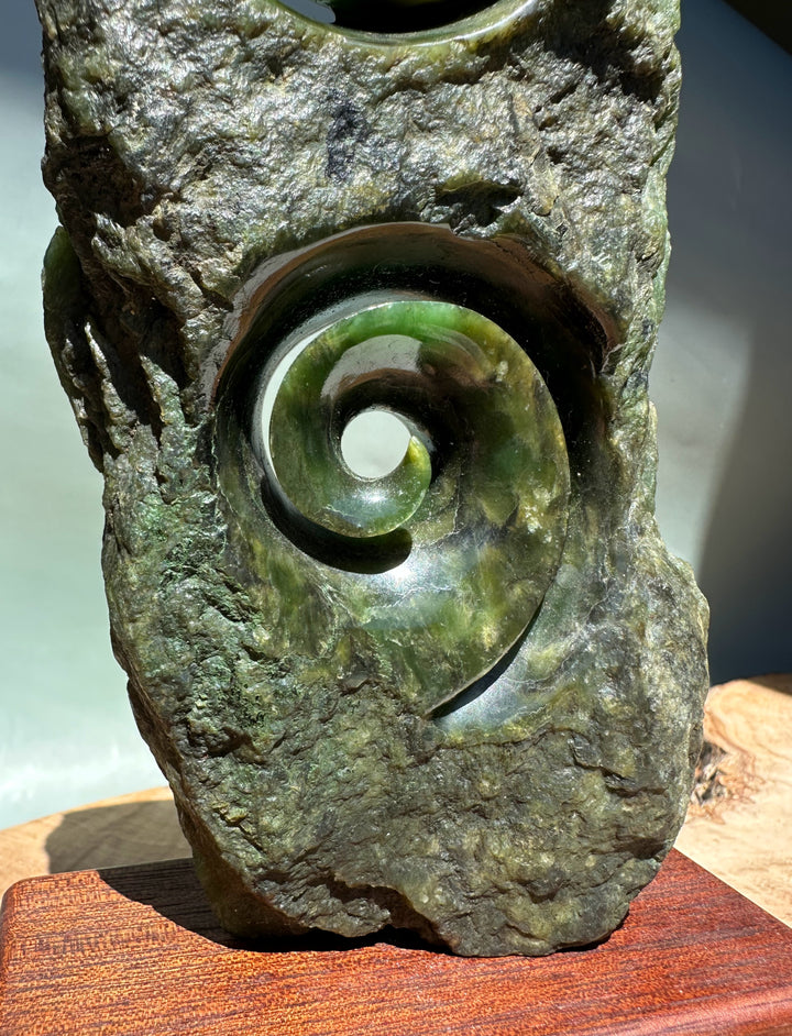 Canadian Jade Double Koru Sculpture 8 inches featuring a glossy green jade spiral set in a rugged rock base on a wooden stand.