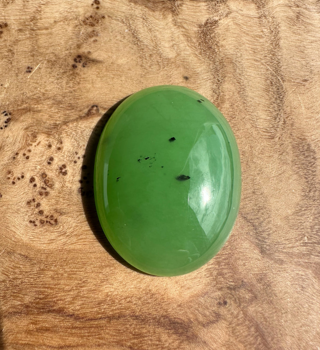 Apple green Siberian cabochon polished oval 30x22 mm with small dark inclusions.