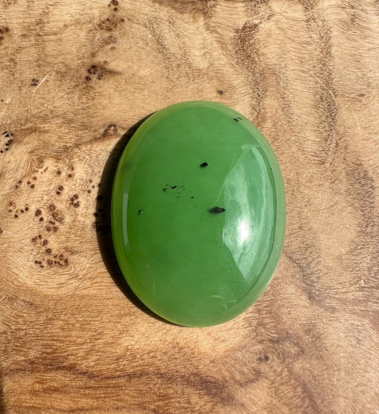 Apple green Siberian cabochon polished oval 30x22 mm with small dark inclusions.