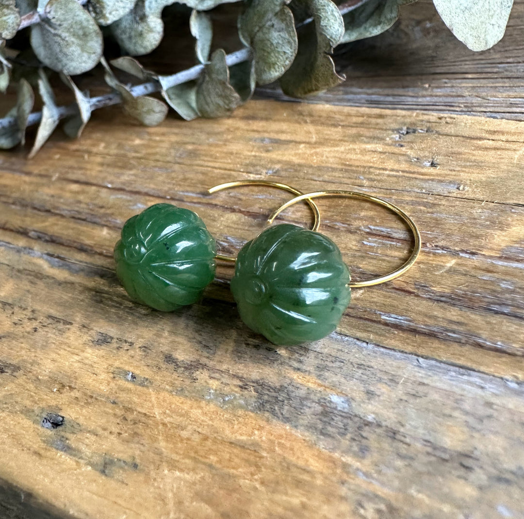Green Canadian Jade drop beads with vertical grooves on gold hoop earrings resting on wood.
