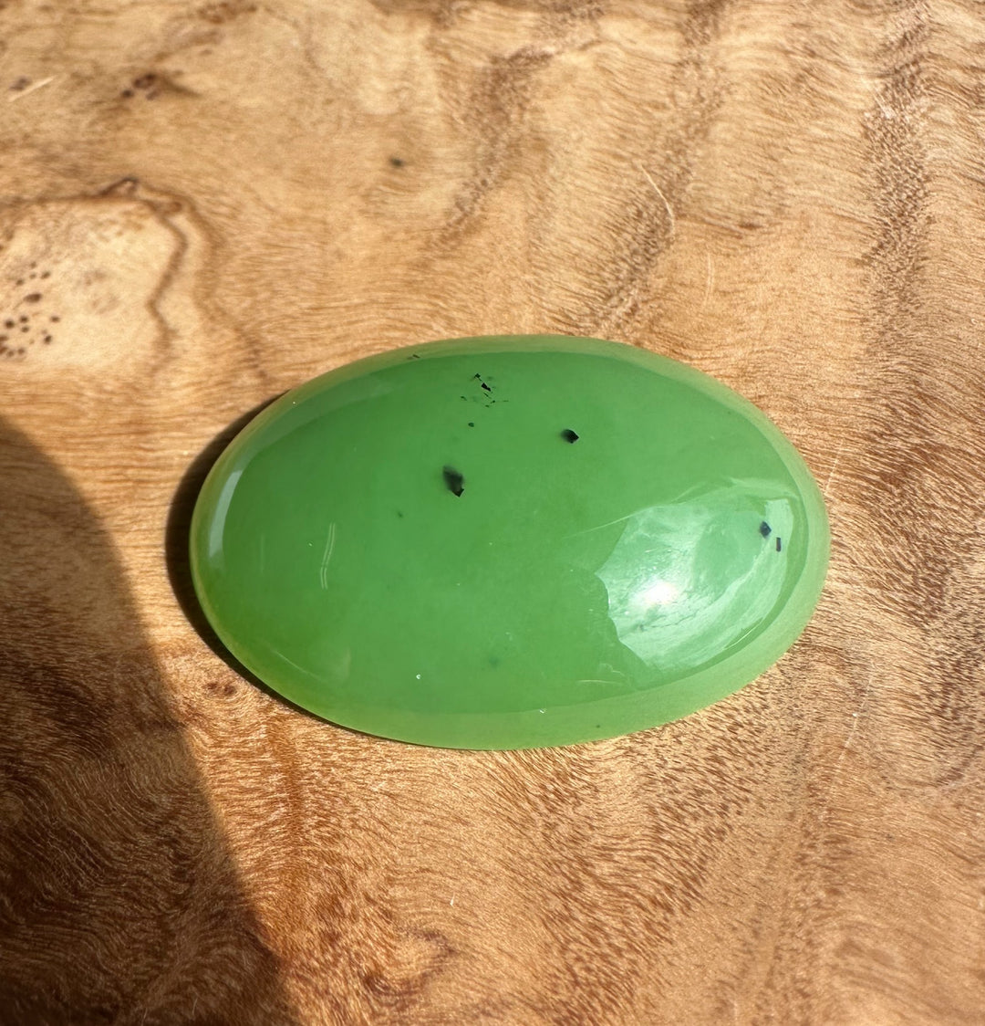 AA Siberian Apple Green Cabochon 30x22mm oval, glossy green gemstone on a wood surface