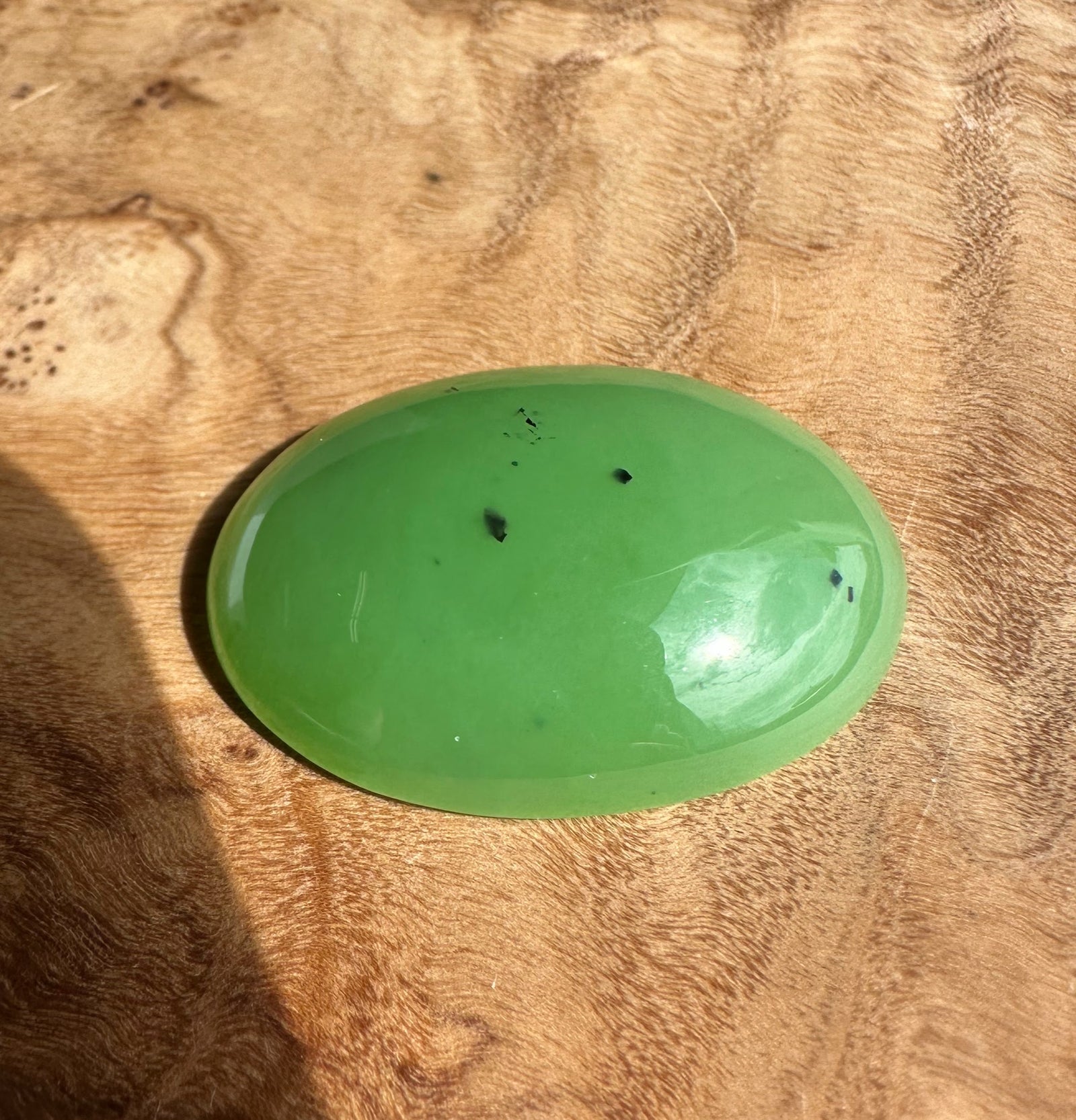 AA Siberian Apple Green Cabochon 30x22mm oval, glossy green gemstone on a wood surface