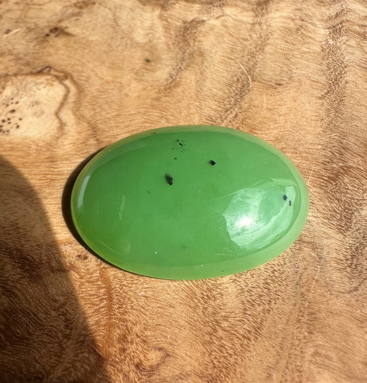 AA Siberian Apple Green Cabochon 30x22mm oval, glossy green gemstone on a wood surface
