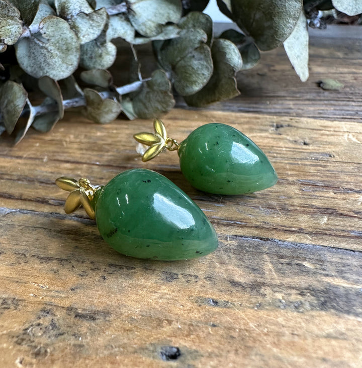 Close-up of green jade teardrop earrings with gold leaf caps resting on a wooden surface